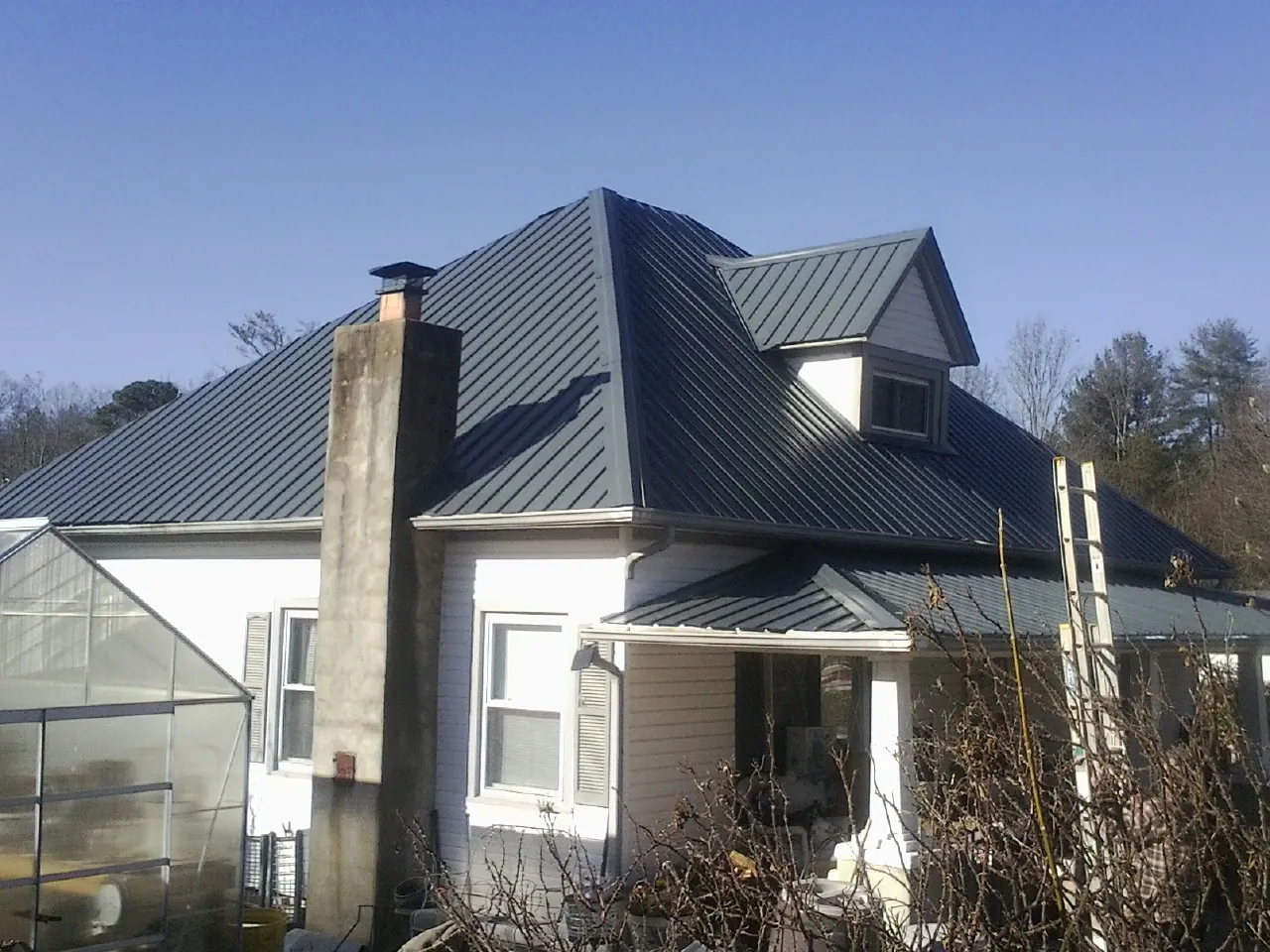 Dark blue standing seam metal roof on a white farmhouse with dormer — Slate & Tile Roof Repair by Roofing Brothers in Bryant