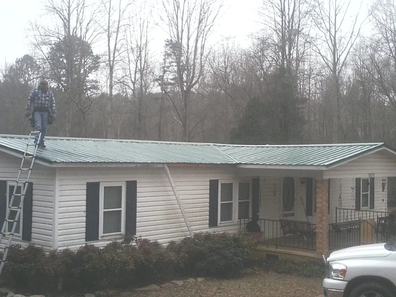 Worker on a ladder beside a new green metal roof on a ranch home in Bryant