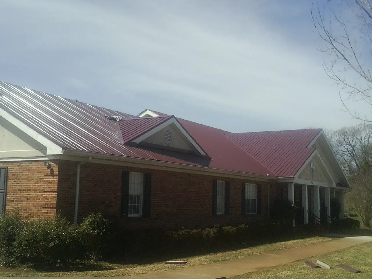 Red metal roof with gabled entries on a long brick building, from a Hail Damage Roof Repair job in Bryant