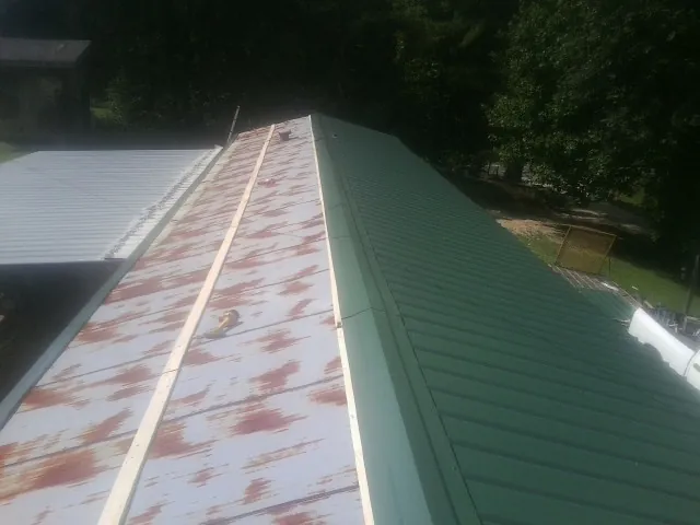 Old rusted panels beside newly installed green metal roofing — Wind Damage Roof Repair by Roofing Brothers in Bryant
