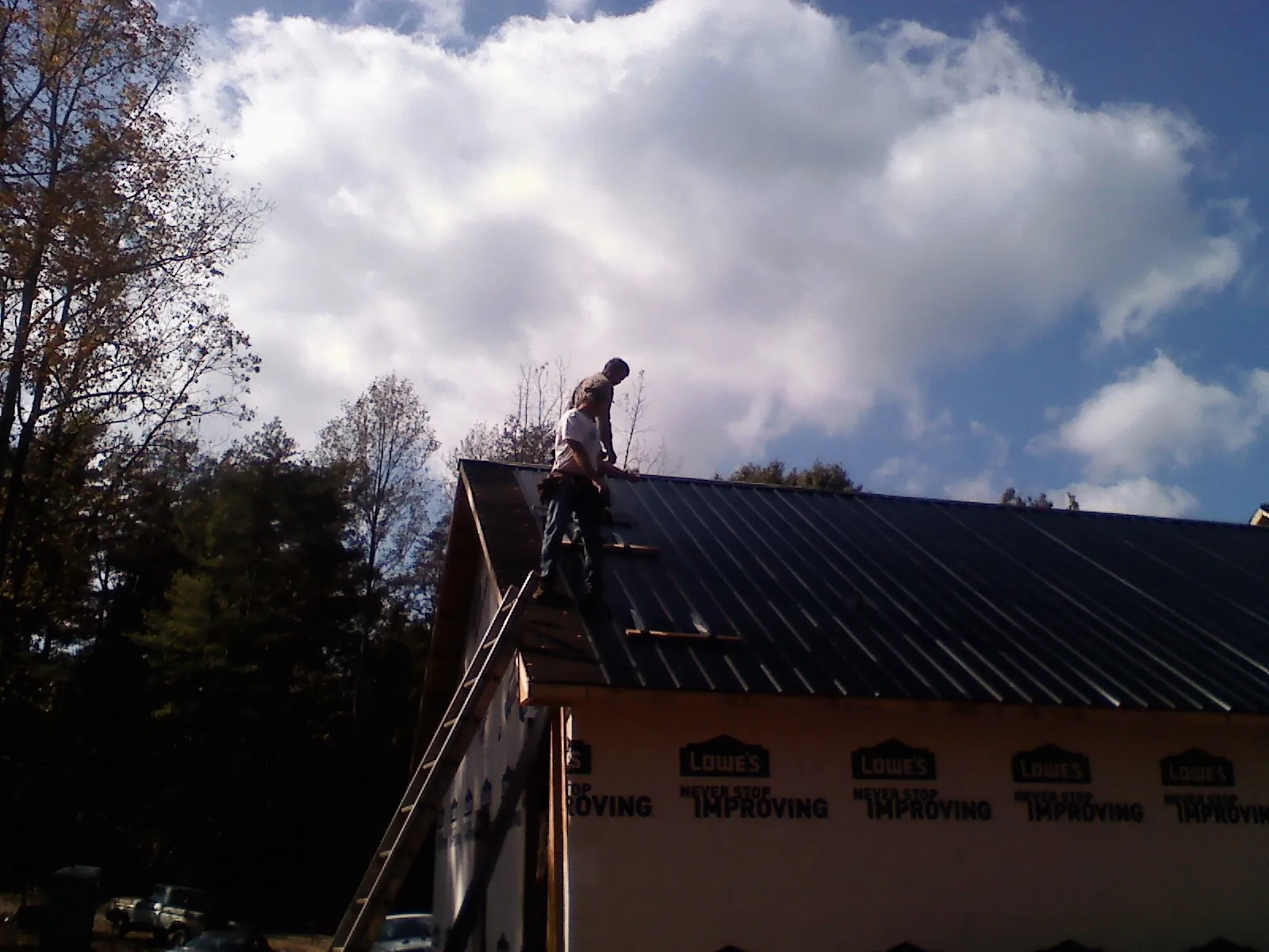 Roofer fastening dark metal panels high against a cloudy sky, from a Roof Inspection job in Bryant