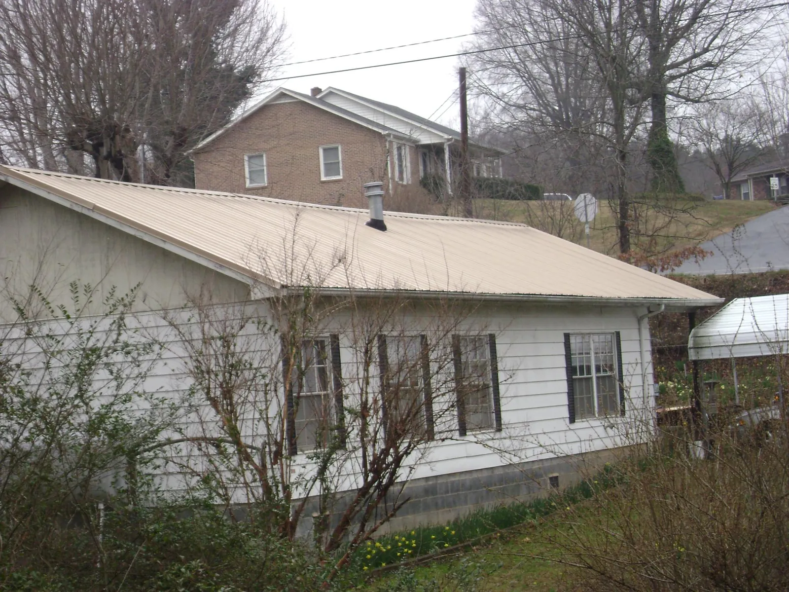 Tan metal roof on a white sided house set into a hillside — Commercial Roofing by Roofing Brothers in Bryant