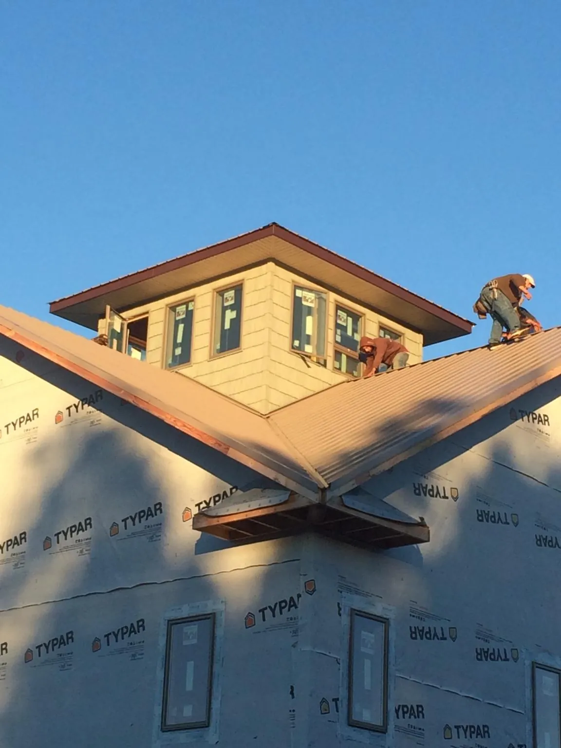 Roofers working around a rooftop cupola on a new metal roof at sunset — Roof Waterproofing in Bryant by Roofing Brothers